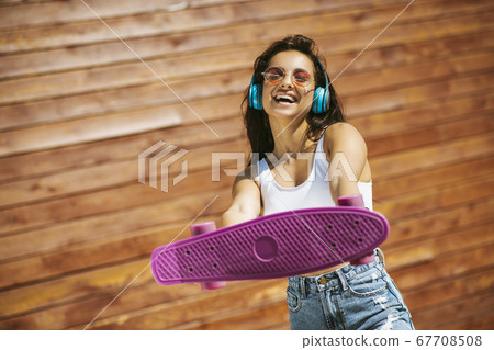 Beautiful brunette girl showing a skateboard and laughing 67708508