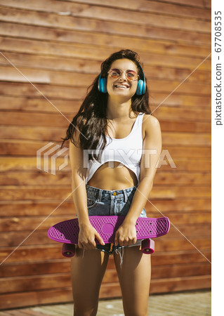 Beautiful brunette girl with skateboard listening to music 67708535