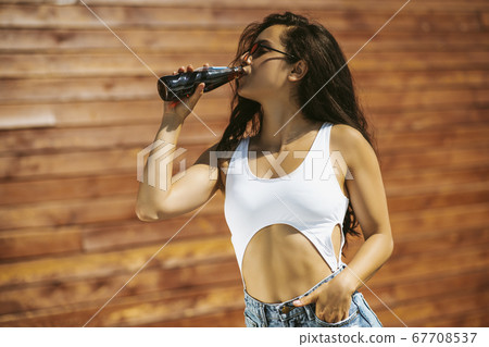 Beautiful brunette girl in white top drinking cola Beautiful brunette girl in white top drinking cola 67708537