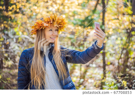 Outdoors lifestyle close up portrait of charming blonde young woman wearing a wreath of autumn leaves. Smiling, walking on the autumn park. Wearing stylish knitted pullover. Wreath of maple leaves 67708853