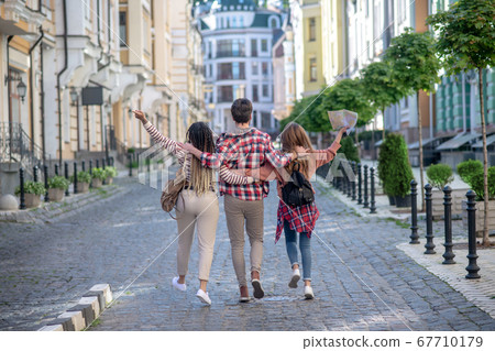 Three young friends hugging walking along the street Three young friends hugging walking along the street 67710179