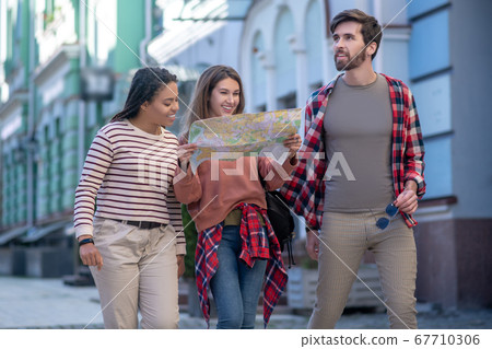 Bearded guy and girls with map walking down street Bearded guy and girls with map walking down street 67710306