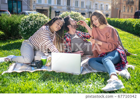 Three friends on a picnic with a laptop 67710342