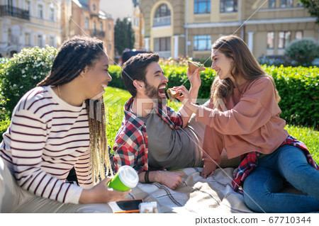 Girl feeding boyfriend sandwich girlfriend with dreadlocks nearby Girl feeding boyfriend sandwich girlfriend with dreadlocks nearby 67710344