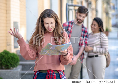 Young adult girl with a map friends nearby. Young adult girl with a map friends nearby. 67710881