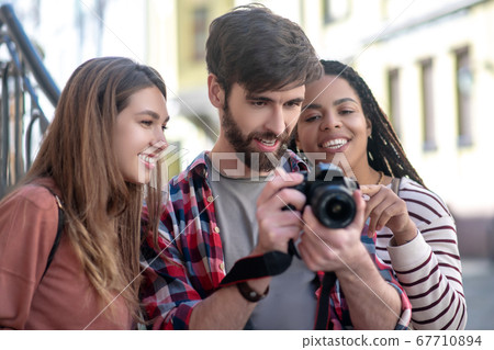 Guy and two girls looking at photos in the camera 67710894