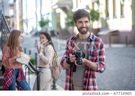 Young adult guy with camera standing on street two girlfriends behind Young adult guy with camera standing on street two girlfriends behind 67710905