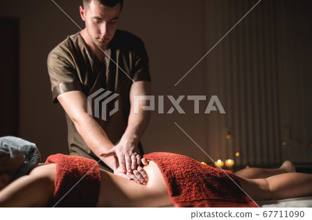 Cosmetology and physiotherapy. Professional massage to the lower back of a woman is made by a masseur man. Concept of manul therapy and massage spa treatments 67711090
