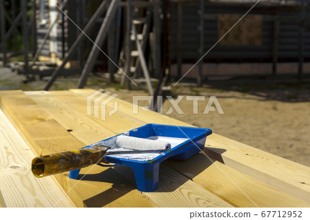 Paint bath with paint roller and white paint on unpainted pine boards 67712952