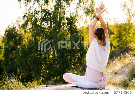 Back view of unrecognizable young woman meditating in lotus position sitting with hands up. Back view of unrecognizable young woman meditating in lotus position sitting with hands up. 67714506