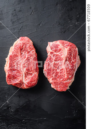 Raw top blade flat Ironcut, on black slate , bio marbled beef with herbs tomatoes peppercorns overblack stone surface background top view space for text vertical 67718509