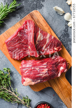 Raw flap steak flank cutHanger steak, bistro steak, fajita meat, on woods chopping board, with herbs tomatoes peppercorns over grey stone surface background top view close up 67718555