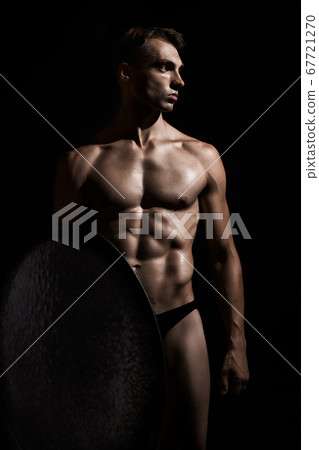 Young warrior with shield isolated on black. 67721270
