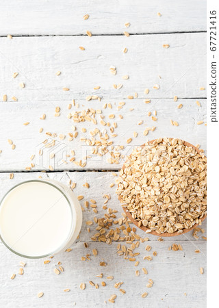 Overhead shot of glass of oat milk on white wooden background with oatmeals in bowl 67721416