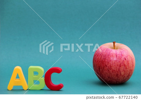 Colored letters of the English alphabet abc next to an apple on a green background.  67722140
