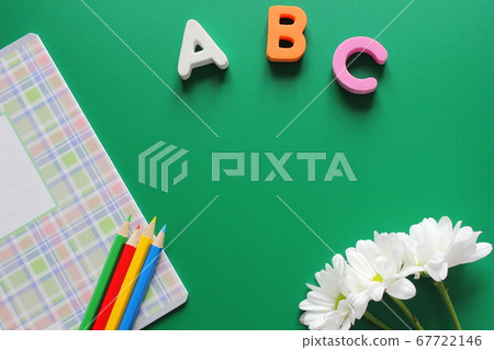 School notebook and colored pencils next to the letters ABC and white chrysanthemums on a green background. School notebook and colored pencils next to the letters ABC and white chrysanthemums on a green background. 67722146