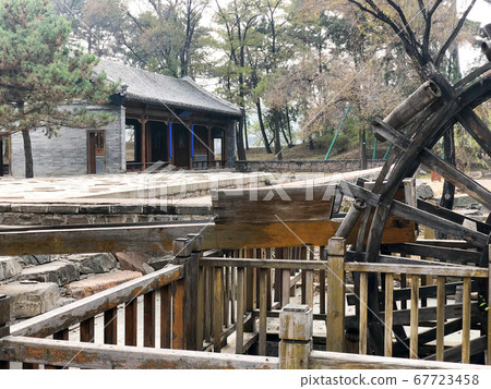 Water mill wheel in a calm little river and little pavilion on the background. China 67723458