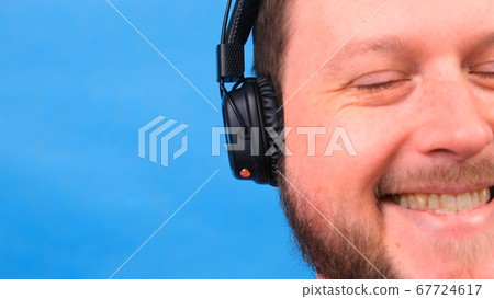 Cheerful charismatic fat man in headphones isolated and pink t-shirt on a blue background. listen to Cheerful charismatic fat man in headphones isolated and pink t-shirt on a blue background. listen to 67724617