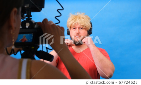 freaky fat man in a wig and a pink t-shirt makes a video blog against a blue background. 67724623