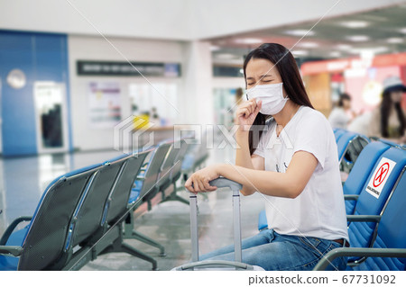 Asian tourist feeling sick, coughing ,wearing mask and sit on chair with social distancing to prevent pandemic during travel at airport terminal. new normal after coronavirus, covid-19 virus epidemic 67731092
