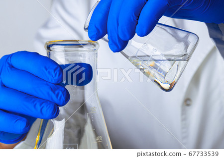 Scientist or doctor in blue gloves pouring some yellow liquid into a flask 67733539