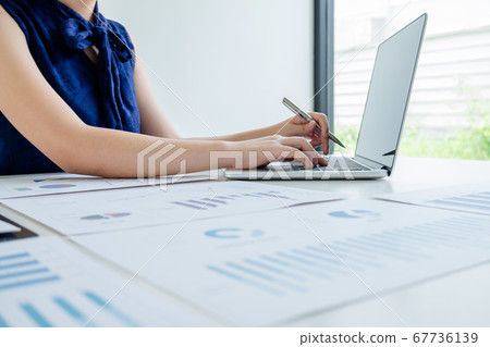 Office girl is sitting at a desk and use laptop calculating financial graph that show results In the office Office girl is sitting at a desk and use laptop calculating financial graph that show results In the office 67736139