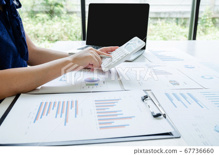 Office girl is sitting at a desk and use calculator calculating financial graph that show results In the office Office girl is sitting at a desk and use calculator calculating financial graph that show results In the office 67736660