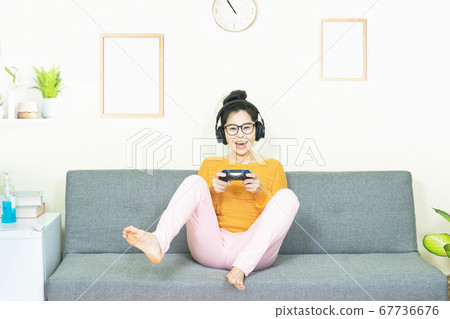people and leisure concept - happy smiling asian young woman with gamepad playing video games on console having fun, resting on weekends at home under quarantine 67736676