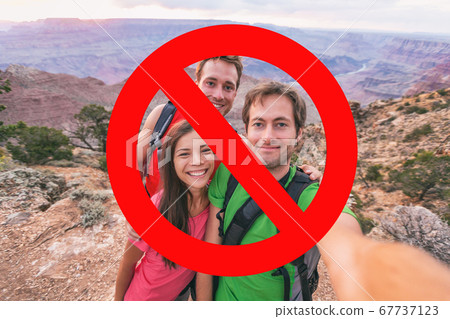 No more selfies. Social distancing obligatory, gatherings forbidden at outdoor hiking nature parks. Group of three friends hikers with red blocked sign overlay No more selfies. Social distancing obligatory, gatherings forbidden at outdoor hiking nature parks. Group of three friends hikers with red blocked sign overlay 67737123