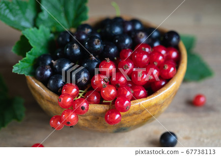 Red and black currant, gooseberry in ceramic bowl on a wooden background 67738113