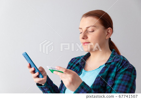 Beautiful young woman online shopping with credit card and smartphone sitting at home. 67741507