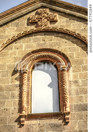 A window covered with a patterned oval cornice and an openwork cross on the Church of St. Mesrop Mashtots in the village of Oshakan 67741644