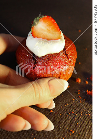 The girl's hand holds a chocolate cupcake decorated with a strawberry slice 67745938
