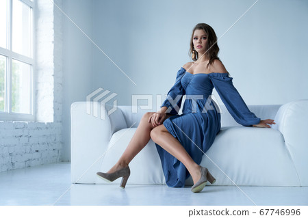 Stylish female model in midi dress on couch. 67746996