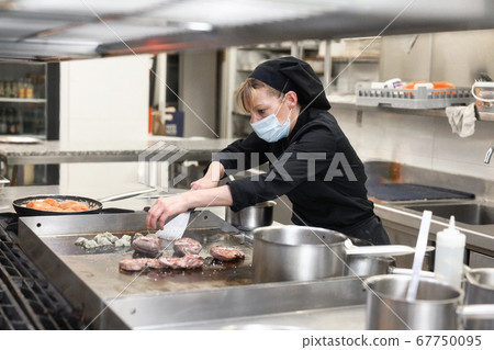 Woman Chef in protective face mask prepare food in the kitchen of a restaurant or hotel. Coronavirus Woman Chef in protective face mask prepare food in the kitchen of a restaurant or hotel. Coronavirus 67750095