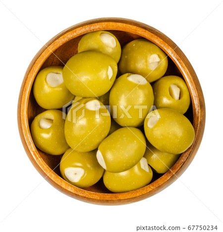 Green olives stuffed with garlic cloves in wooden bowl. Big olives, fruits of Olea europaea, hand filled with pickled garlic pieces. Closeup from above, on white background, isolated macro food photo. 67750234