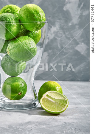 glass vase full of green limes on concrete background 67751441