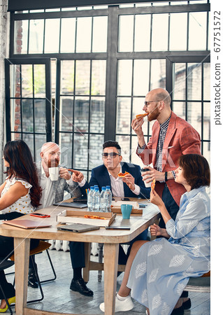 business, food, lunch and people concept - happy international business team eating pizza in office. Outsider on the office team business, food, lunch and people concept - happy international business team eating pizza in office. Outsider on the office team 67751572