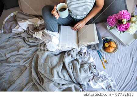 Woman sitting in bed reading a book and having breakfast. Top view Woman sitting in bed reading a book and having breakfast. Top view 67752633