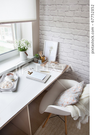 Work table near the window in the Scandinavian Nordic style. Female work and home office concept. White and gold office. Flowers in a vase and rings, bracelets on the table. Work table near the window in the Scandinavian Nordic style. Female work and home office concept. White and gold office. Flowers in a vase and rings, bracelets on the table. 67752852