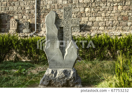 A stone cross made of basalt was carved as a gift to the monastery and installed in a Park near the stone wall near the Geghard monastery in Armenia. A stone cross made of basalt was carved as a gift to the monastery and installed in a Park near the stone wall near the Geghard monastery in Armenia. 67753232