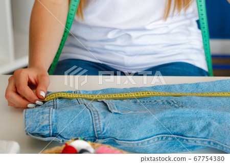 Woman tailor making measurements with measuring tape in her office 67754380