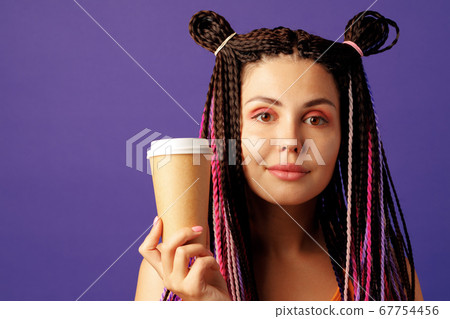 Young caucasian woman with colorful long cornrows holding a cup of coffee against purple background 67754456