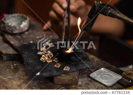 A person is melting silver to make jewellery. A person is melting silver to make jewellery. 67761334