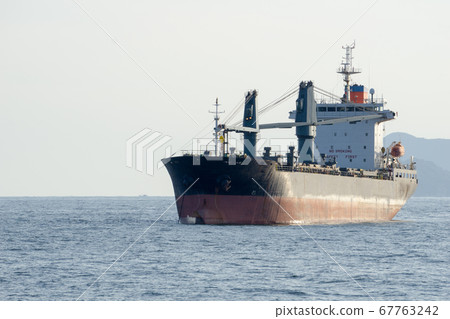 Old commercial cargo ship with heavy cranes anchors in the sea Old commercial cargo ship with heavy cranes anchors in the sea 67763242