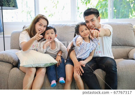 Asian father sitting on sofa in living room watching their favourite TV show at home 67767317