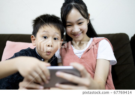 Excited kid boy and child girl are enjoying playing online game on mobile phone,siblings having fun relaxing together,children sister and brother using smartphone to watch cartoon video,stay home