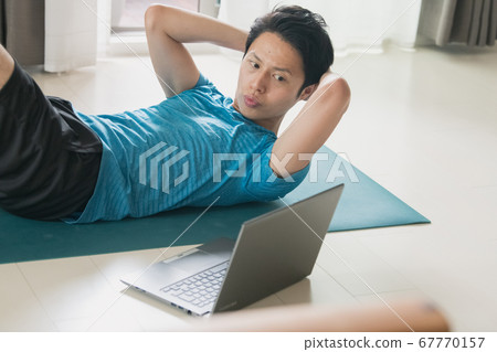 Image of a man doing muscle training, abdominal muscles and core training while looking at the PC Image of a man doing muscle training, abdominal muscles and core training while looking at the PC 67770157
