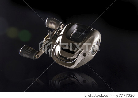 Golden fishing reel placed on a reflection area Golden fishing reel placed on a reflection area 67777026