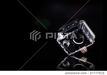 action cam is placed on a reflective area. With light shining from the side to the black background 67777616